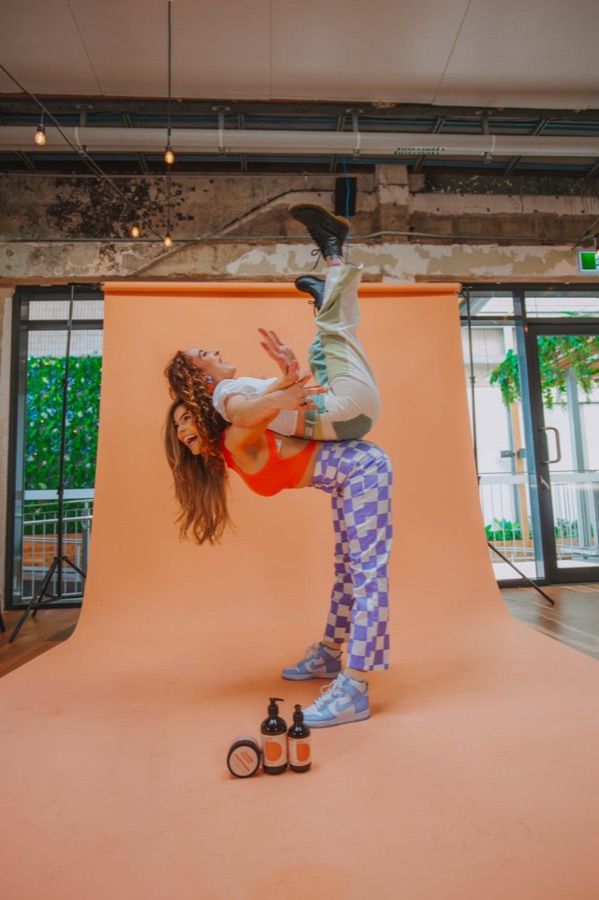 A product shoot on a peach backdrop with a model mid-handstand